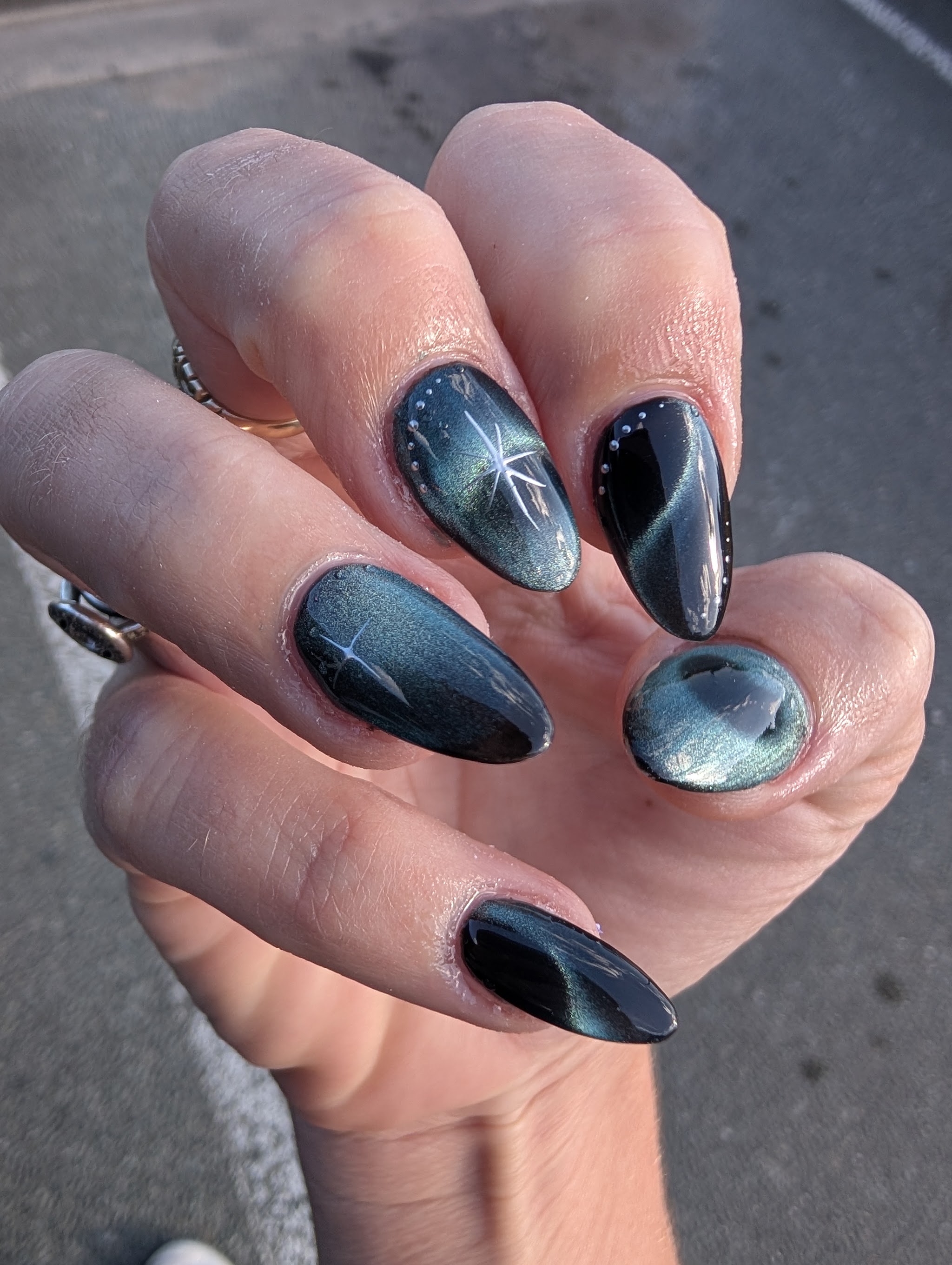 Dark teal and black chrome cat-eye nails with starburst detail